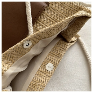 Detail of woven tote bag showing magnetic clasp and natural straw texture with leather trim