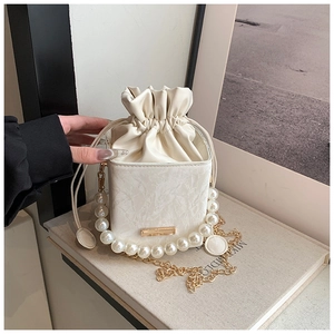 Detail of cream white bucket bag with pearl handle, gold chain and marble texture finish