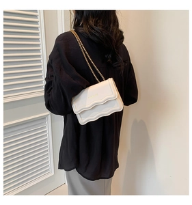 Close-up of white crossbody bag with wavy flap edge and gold chain strap detail