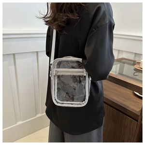 Close-up of a clear PVC crossbody bag featuring silver zippers and adjustable white strap