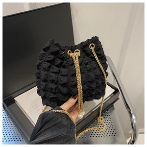 Detail of black bubble texture bucket bag with gold chain strap and pearl accents