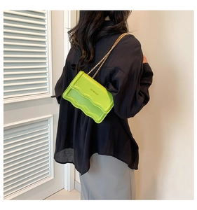 Detail of neon green textured small square bag with metallic chain strap worn by a model