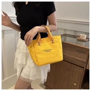Détail du sac seau en toile jaune vif avec texte tendance et accents de rivets métalliques