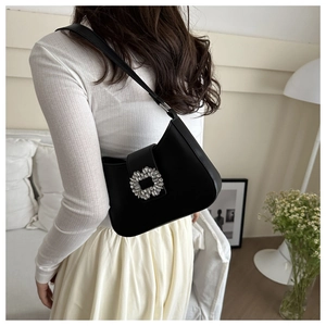 Detail view of black underarm bag featuring a crystal rectangle buckle on a matte shoulder bag