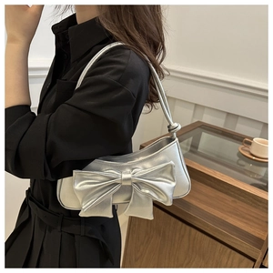 Silver bow shoulder bag with metallic finish shown on model in casual indoor setting