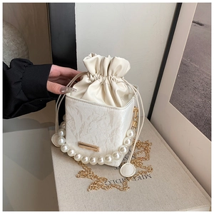 Detail of white pleated bucket bag with pearl handle and golden chain strap