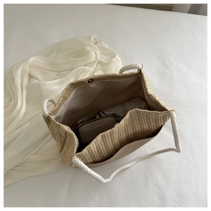 Macro view of woven straw tote bag featuring white cotton handles and magnetic clasp
