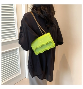 Detail of neon green leather crossbody bag with wavy flap design and gold chain strap