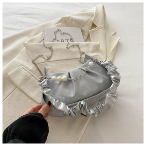 Silver pleated cloud bag with metallic chain and pearl accents on a beige blazer