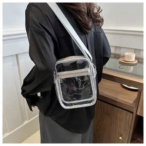 Transparent PVC crossbody square bag with silver grey strap worn by a model in a cafe
