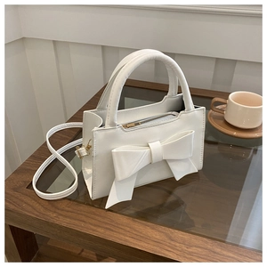 Detail of white rectangle handbag featuring a large leather bow and metal zipper closure