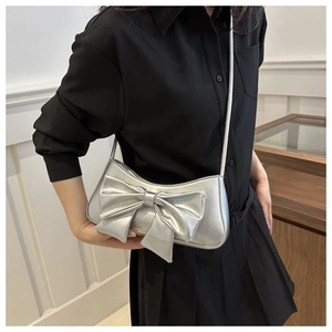 Detail shot of a silver metallic underarm bag with a large 3D bow accent on model