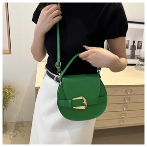 Detail of green leather saddle bag featuring a large gold buckle and smooth texture