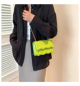 Detail of light green crossbody bag with wavy flap design and golden chain strap