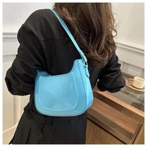 Sky blue patent leather half-moon shoulder bag styled on model in minimalist interior