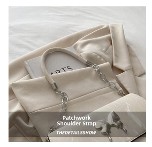 Detail shot of a silver butterfly emblem on a cream shoulder bag with chain strap