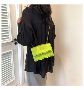 Detail of neon green chain bag with wavy flap edge and gold strap on model