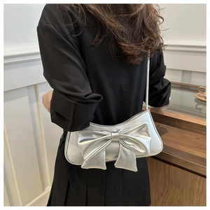 Detailed view of silver metallic bow shoulder bag with glossy texture on model