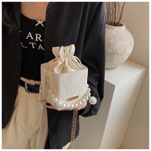 Detail of white drawstring bucket bag with elegant pearl handle and gold chain strap