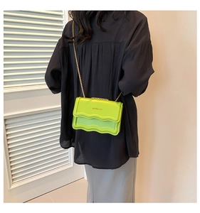 Detail of neon green scalloped edge shoulder bag with golden chain and metallic logo