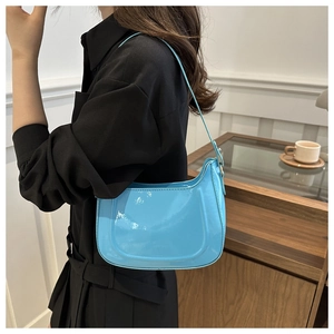 Detailed view of sky blue glossy patent leather crossbody bag with slim strap on shoulder