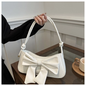 Detail of white crocodile pattern shoulder bag featuring a large bow and gold hardware