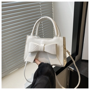 Detail of white mini handbag featuring a large bow and adjustable shoulder strap