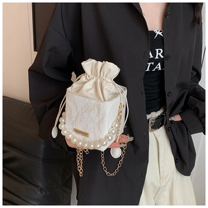 Detail of white drawstring bucket bag featuring a large pearl handle and gold chain accents