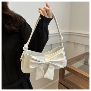Detailed view of white faux crocodile shoulder bag with oversized bow and knotted strap