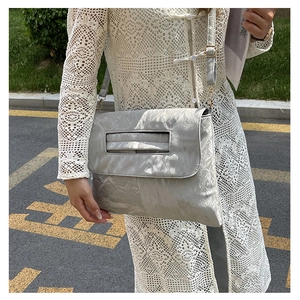 Detail of silver metallic PU crossbody bag with pleated texture worn by model