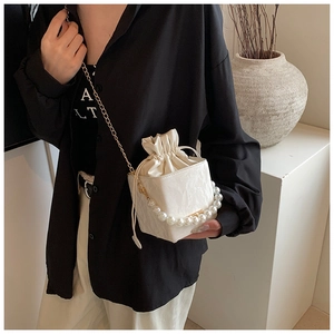 Détail du sac boîte blanc avec poignée en perles et chaîne dorée porté par un mannequin