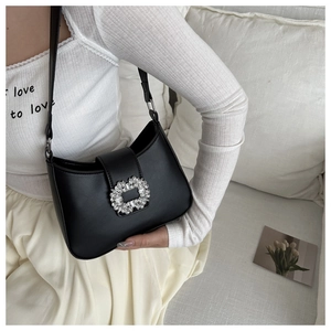 Detail of a black leather underarm bag with a sparkling rhinestone buckle on a model