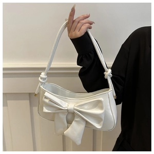 Close-up of white leather underarm bag featuring a large bow and knotted handle detail