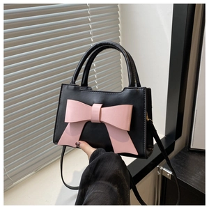 Detail of black crossbody bag featuring a large pink bow and elegant gold zipper