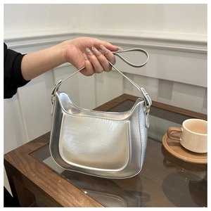 Detail of silver metallic crescent bag with glossy finish and gold hardware accents