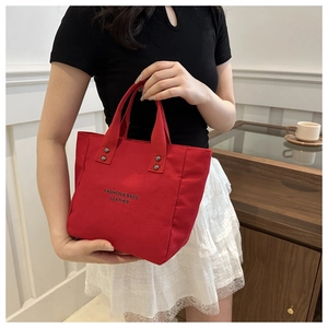 Détail d'un sac seau en toile rouge avec logo noir et rivets métalliques sur la poignée