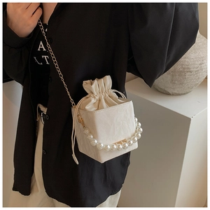 Detail of off-white bucket bag with large pearl handle and elegant gold chain strap