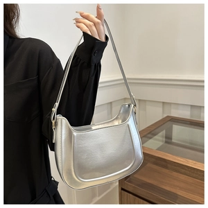 Close-up of a silver mirror finish hobo bag with gold buckle hardware held by a model