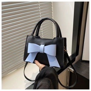 Detail of black handbag featuring a large 3D light blue bow and sleek top handle