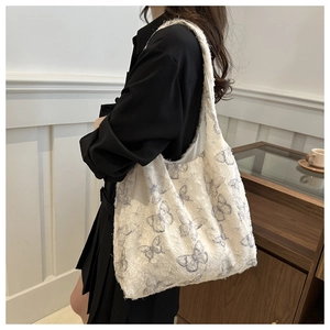 Detail of white velvet tote bag with blue butterfly embroidery shown on model shoulder