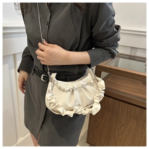 Detail of creamy white pleated handbag with decorative pearl and floral metal chain