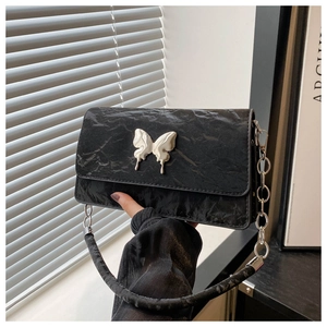 Macro detail of black quilted shoulder bag with silver butterfly buckle and chain strap