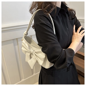 Close-up of cream underarm bag featuring a large bow and knotted shoulder strap detail