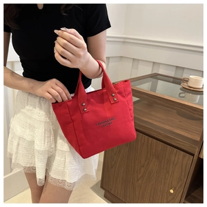 Détail du sac cabas en toile rouge avec lettrage noir et rivets métalliques sur les anses