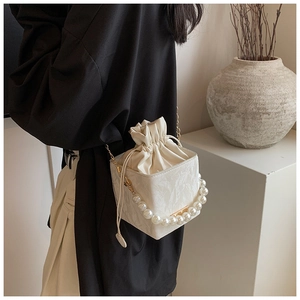 Detail of white textured bucket bag featuring pearl handle and gold chain strap
