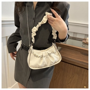 Detail of cream pleated crossbody bag featuring pearl heart chain and ruffled strap