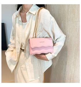 Detail of pink leather crossbody bag with wavy edge flap and gold chain strap