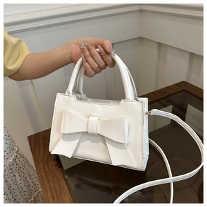 Detail of white handbag featuring a large 3D bow decoration and sleek leather texture