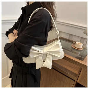 Detailed view of cream leather shoulder bag with a large bow on black dress model