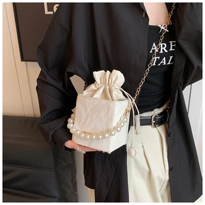 Detail of cream mini bucket bag with large pearl handle and gold chain strap on model